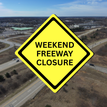 Blurred drone shot of bridge over freeway with yellow caution sign in forefront
